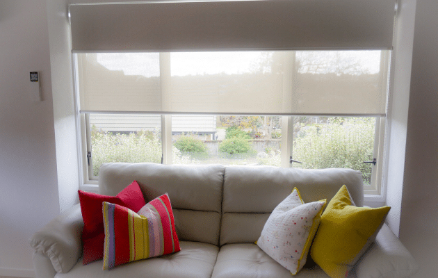 A white couch in front of a window recess that has a dual double roller blinds Auckland.