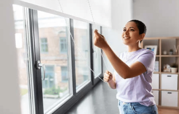 A smiling woman is pulling a roller blind Auckland chain.