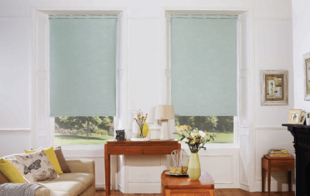 A white lounge wall showing two pale green thermal roller blinds Auckland rolled 3/4 down, from Home Vision Blinds.