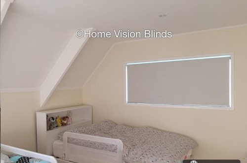 A Home Vision Blinds client's cream coloured child's bedroom showing a rectangle beige blackout roller blind Auckland effectively blocking out the light.