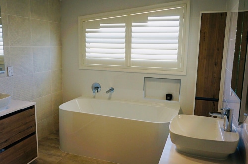 Home Vision Blinds client's bathroom that are showcasing white shutter blinds as an alternative to roller blinds Auckland.