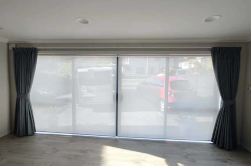 Home Vision Blinds Client's lounge with a wall of windows covered with sunscreen roller blinds Auckland to filter the natural light.
